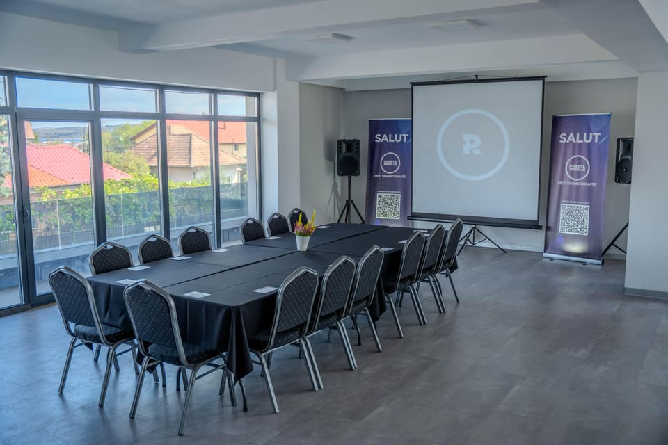 The same hall with the tables pushed together into one long table ringed with chairs, beside the glass wall.